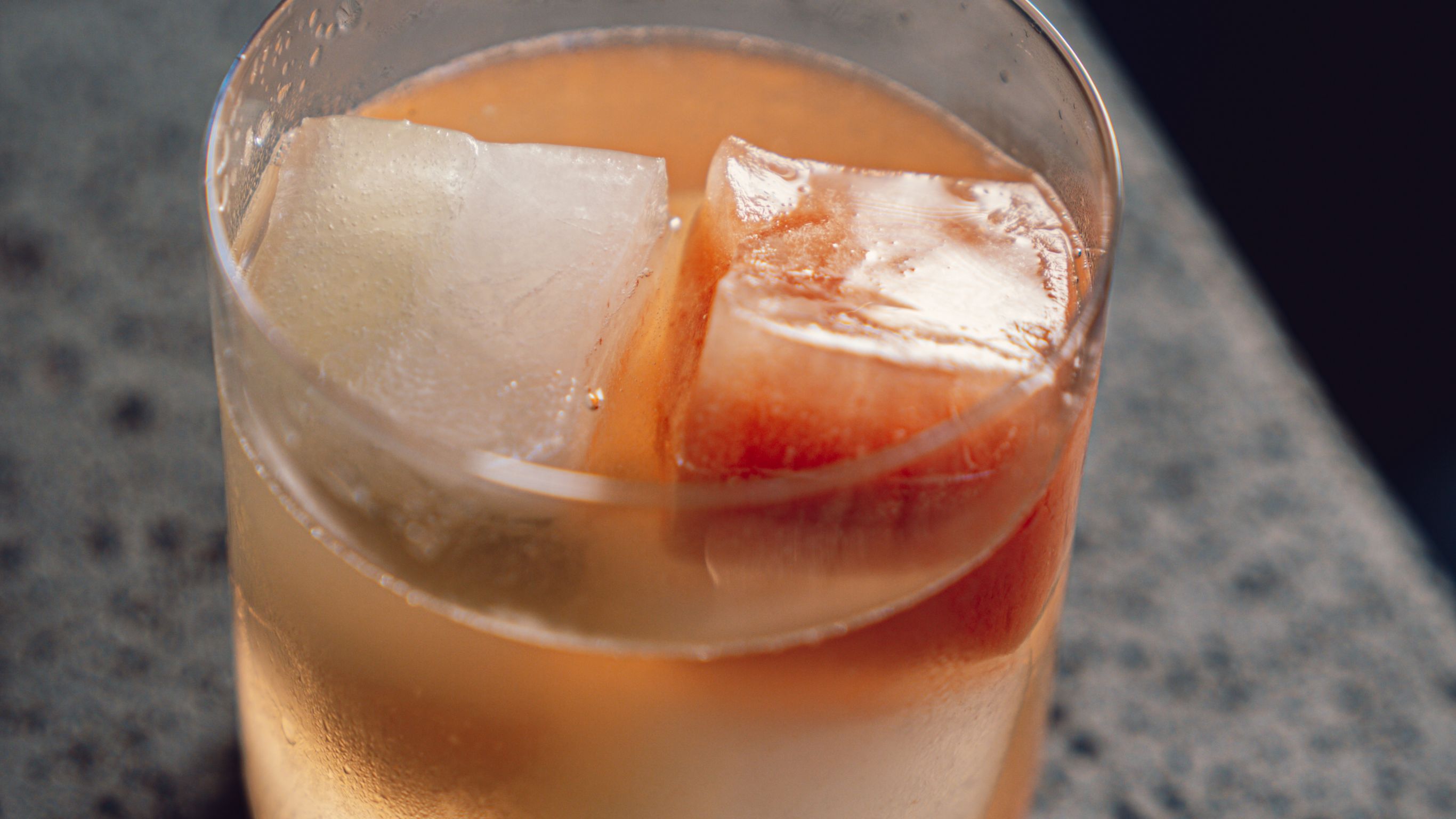 Cóctel rosa claro en vaso de rocas con cubo de hielo sobre mesa de piedra